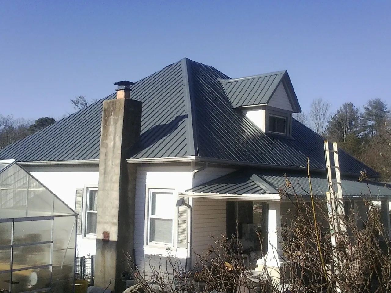 Dark blue standing seam metal roof on a white farmhouse with dormer — Slate & Tile Roof Repair by Roofing Brothers in Fosston