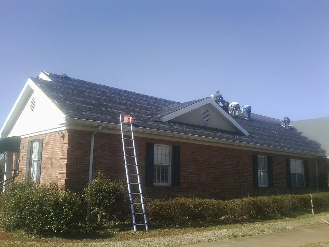 Crew tearing shingles off a brick ranch roof with a ladder set — Emergency Roof Repair work by our crew in Fosston