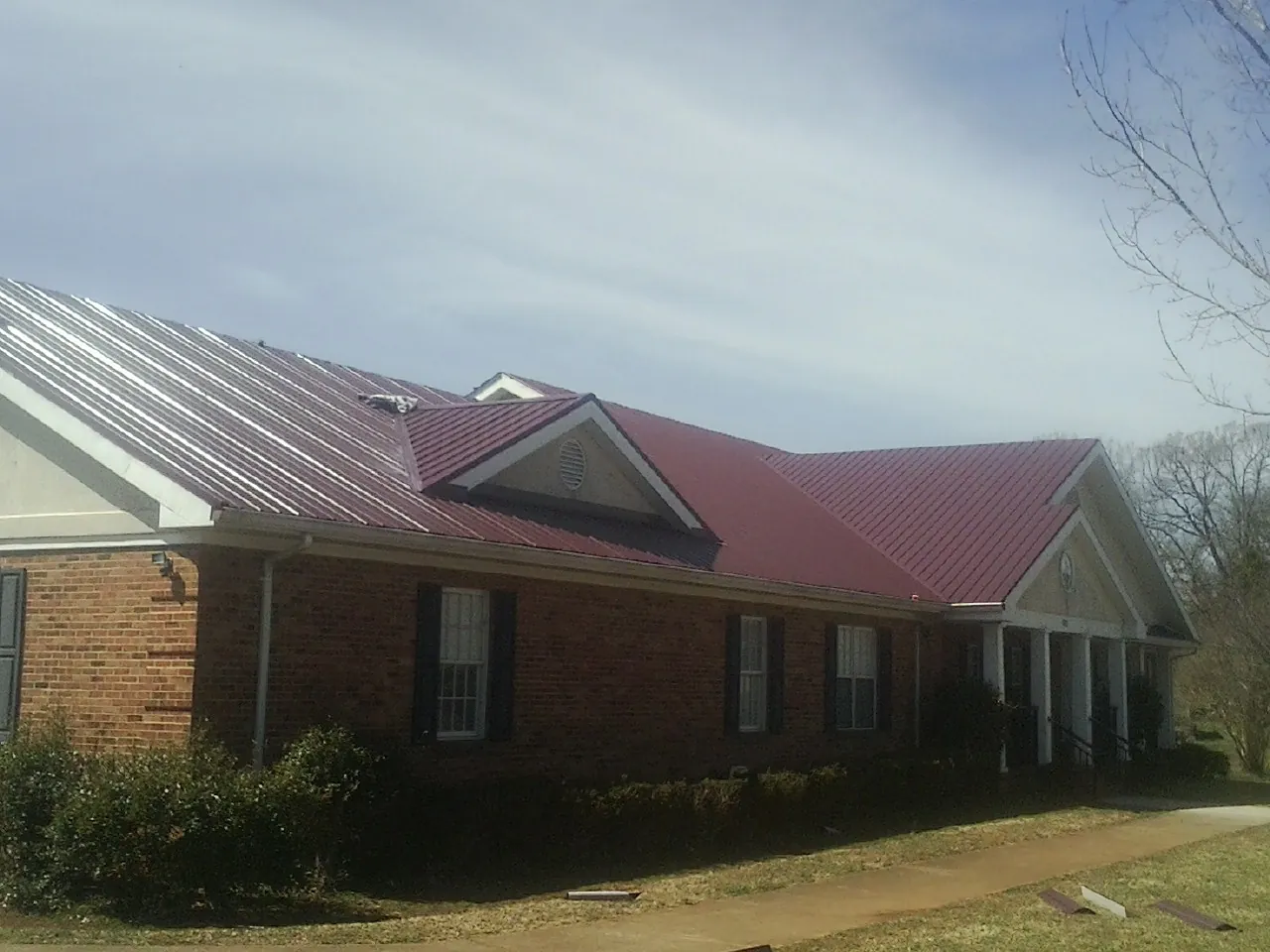 Red metal roof with gabled entries on a long brick building, from a Hail Damage Roof Repair job in Fosston