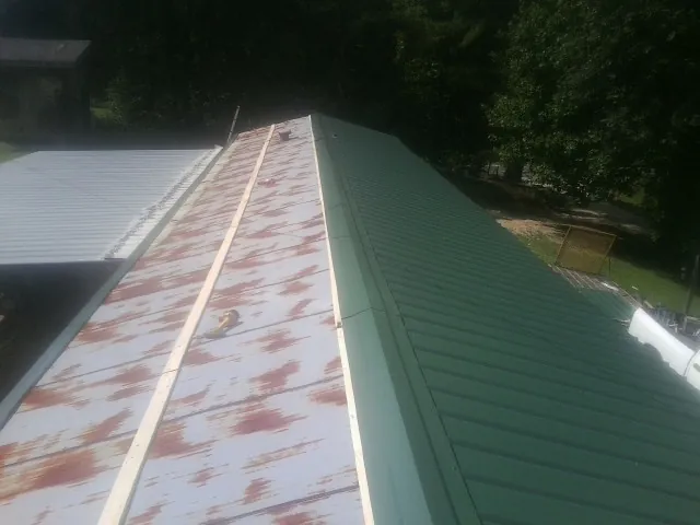 Old rusted panels beside newly installed green metal roofing — Wind Damage Roof Repair by Roofing Brothers in Fosston