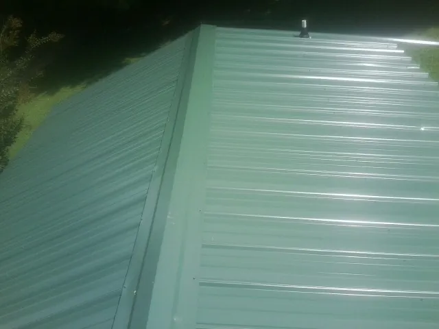 New green metal panels meeting at the ridge of a roof — Flat Roof Repair work by our crew in Fosston