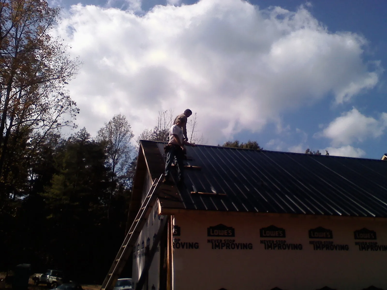 Roofer fastening dark metal panels high against a cloudy sky, from a Roof Inspection job in Fosston