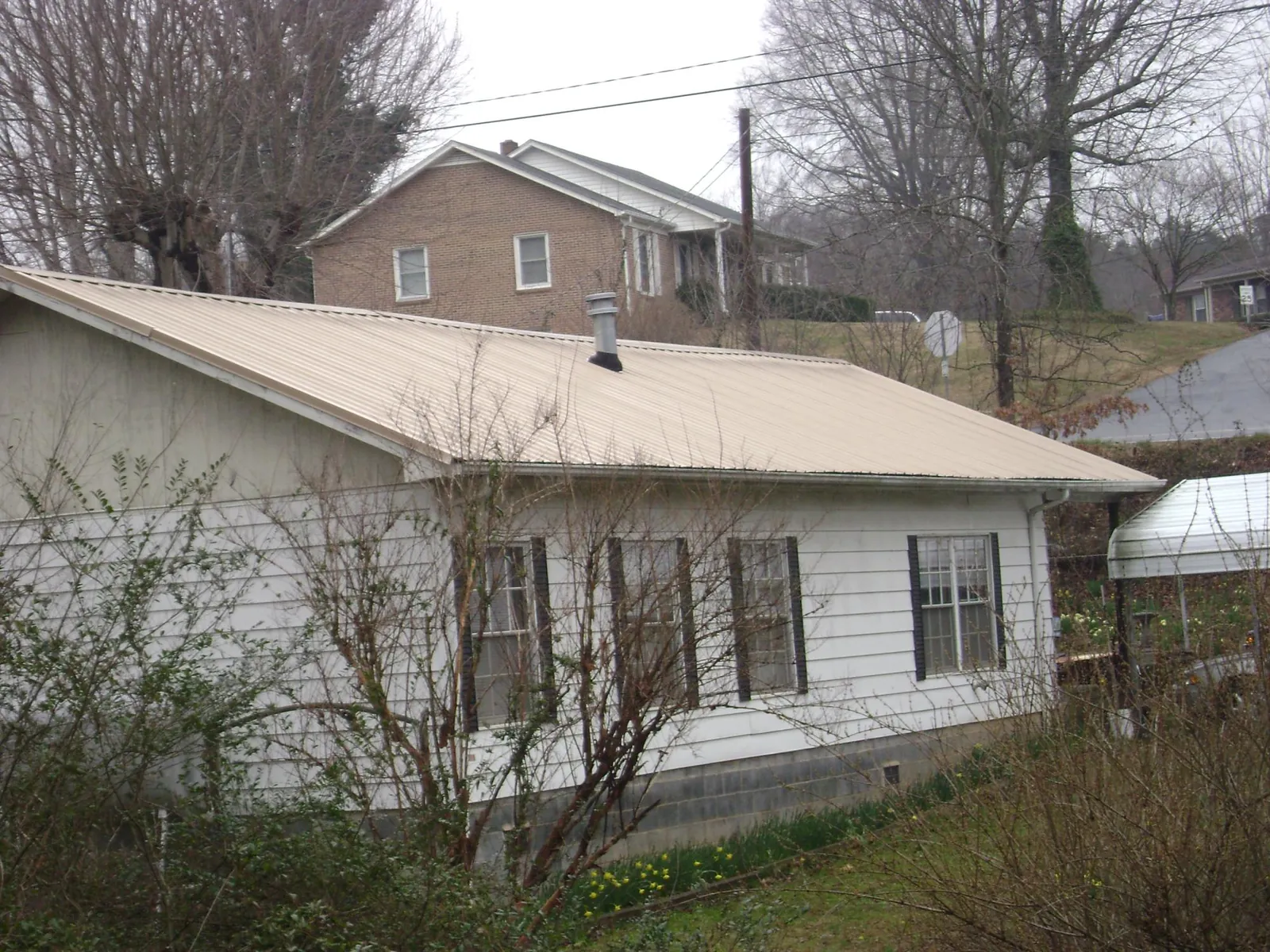 Tan metal roof on a white sided house set into a hillside — Commercial Roofing by Roofing Brothers in Fosston